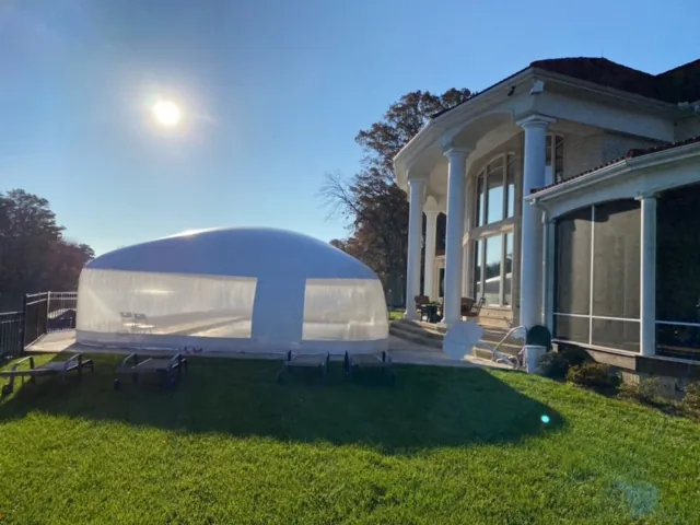 Clear pool dome enclosure tucked against a large columned house