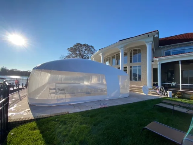 Clear pool dome enclosure beside a lakefront home with seating visible inside
