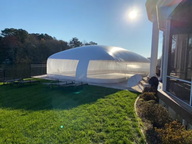 Clear pool dome enclosure on a lawn in morning sun with loungers outside