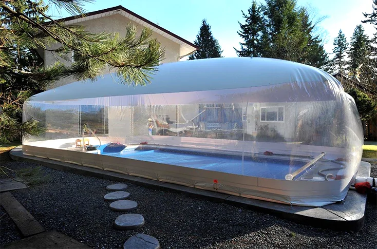 Clear pool dome enclosure over a rectangular backyard pool beside a house