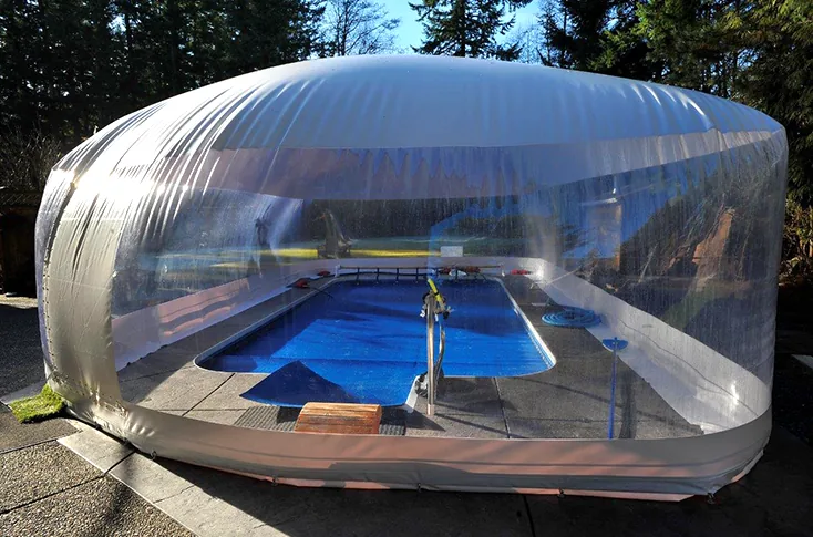 Clear-walled pool dome enclosure backlit by afternoon sun over a backyard pool