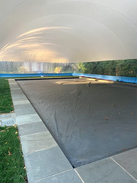Interior of a pool dome enclosure with the pool under a winter cover and a clear window band above