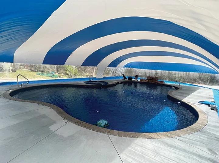 Inside a blue and white striped pool dome enclosure showing a freeform pool and the clear window band