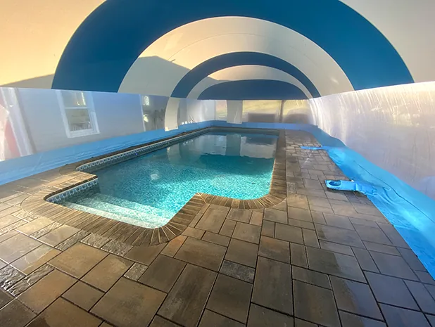 Interior of a blue and white striped pool dome enclosure in the evening over a paver deck
