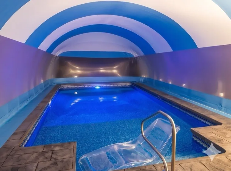 Interior of a blue and white striped pool dome enclosure lit at night with a lounger at the pool edge