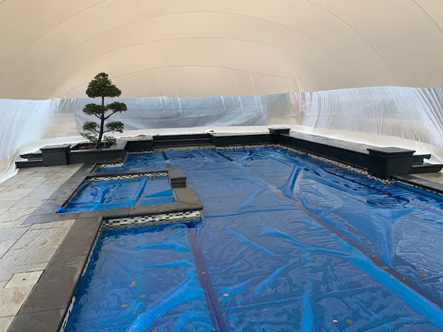 Interior of a tan-roofed pool dome enclosure throwing warm light across the deck