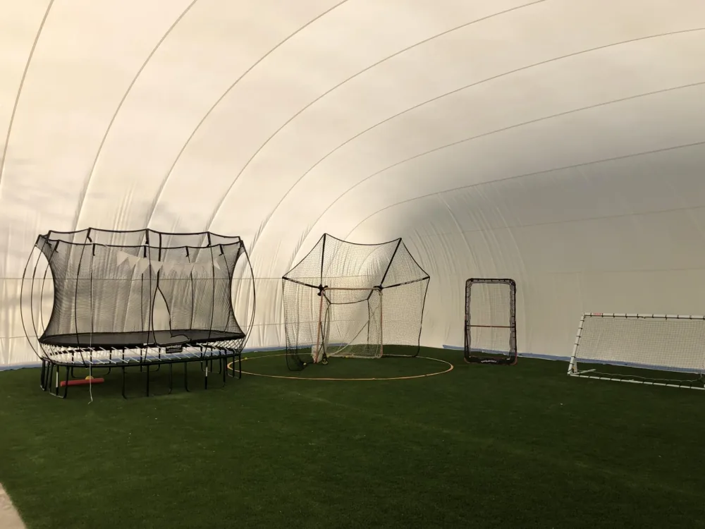 Inside a large white dome over artificial turf with a trampoline, batting cage and soccer goal