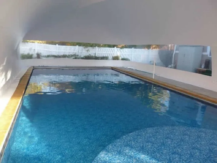 Interior of a white pool dome enclosure with the clear window band framing the yard outside