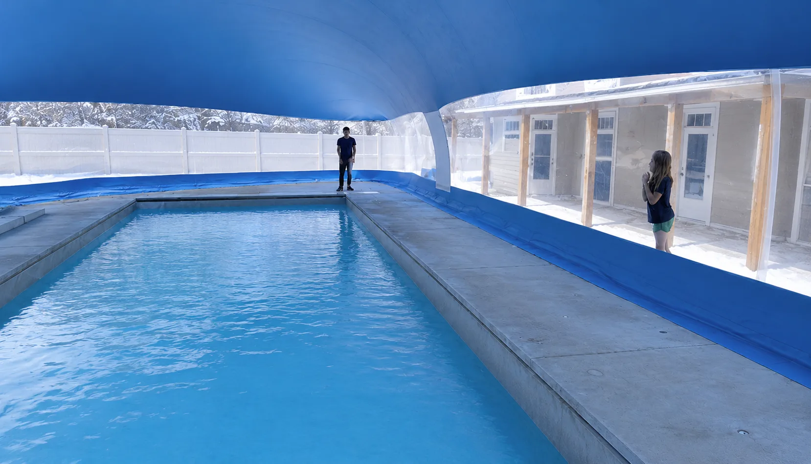 People swimming inside an air-supported pool dome enclosure while snow sits outside the translucent walls