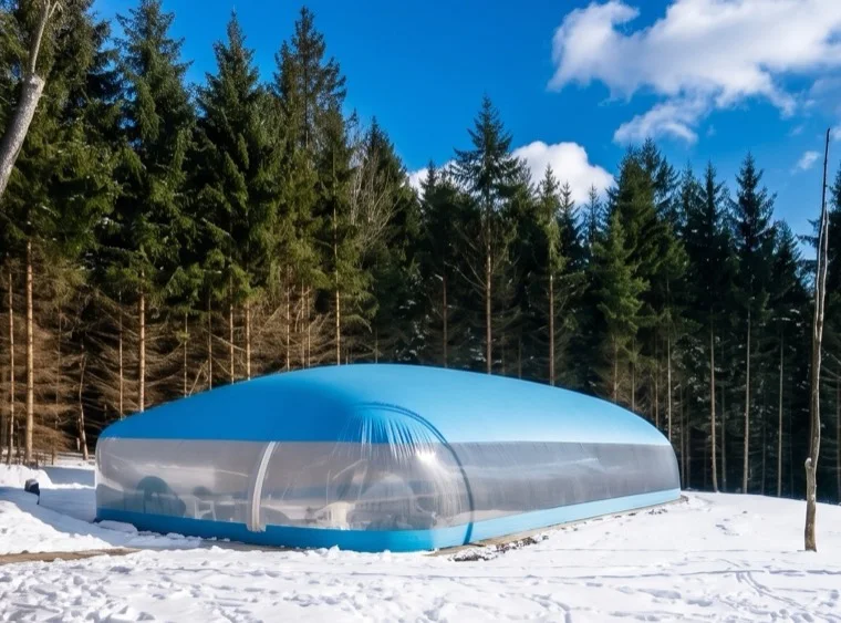 Aqua-roofed pool dome enclosure in deep snow ringed by pine trees