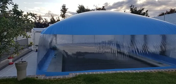 Solid blue pool dome enclosure at dusk showing the clear window band