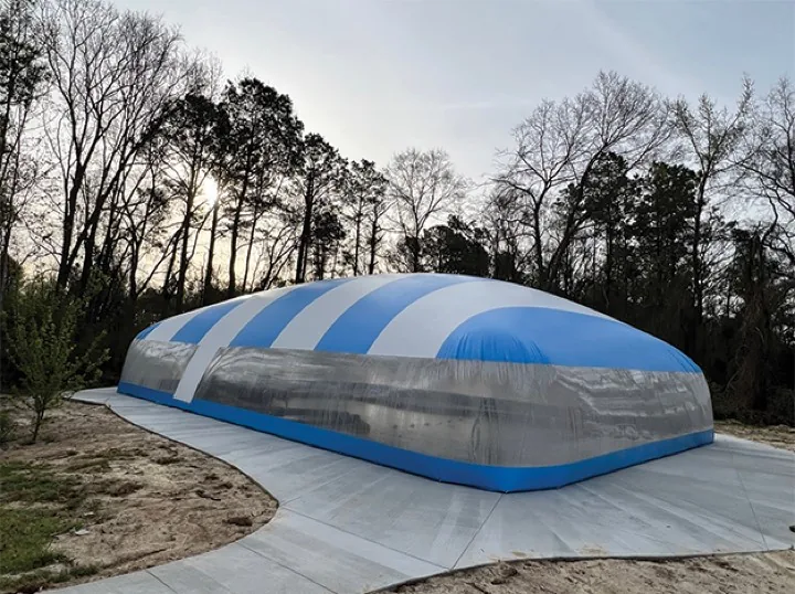 Blue and white striped pool dome enclosure at dusk on a newly poured deck