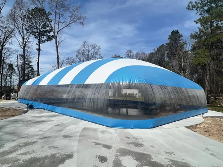 Blue and white striped pool dome enclosure under full sun on a new concrete deck