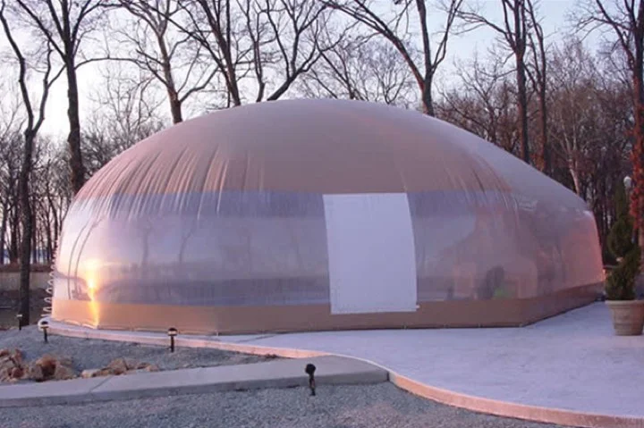 Tan-roofed pool dome enclosure glowing at dusk beside a concrete walkway
